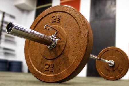 Barbell with red weight plates 10 kg for crossfit training and metal locks, in the hall. Blurred...