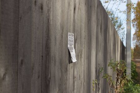 A paper ad with loose leaves is glued to a wooden fence in the countryside. In the background, a concrete pillar and blue sky.
8の写真素材