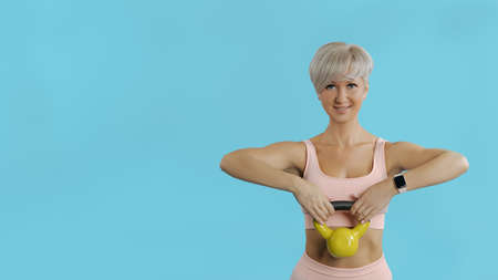 Beautiful athletic woman holding yellow kettlebell COPY SPACE BLUE BG