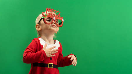 Toddler girl in red Christmas costume and glasses smiling on green background COPYSPACEの写真素材
