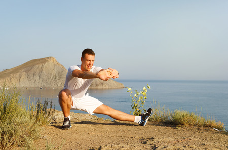 handsome athlete warming up before jogging on the sea backgroundの写真素材