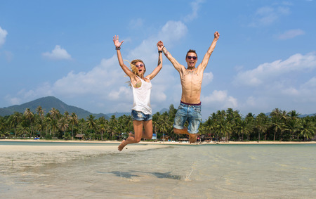 couple bounces cross-legged on the beach holding hands and lifting them upの写真素材