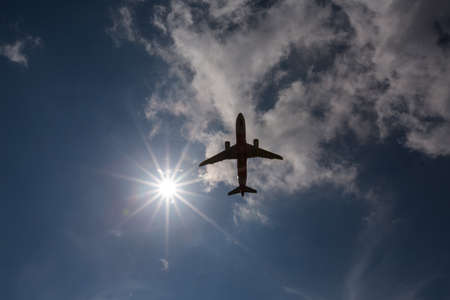 Airplane silhouette in the sky with sun and clouds aroundの写真素材
