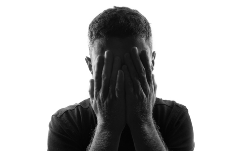 Male person silhouette over white covering his face with handsの写真素材
