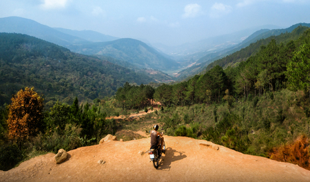 Shot of adventurer enjoy touring motorbike stopped by a cliff viewpoint on mountain peak with pine forest in Vietnamの写真素材