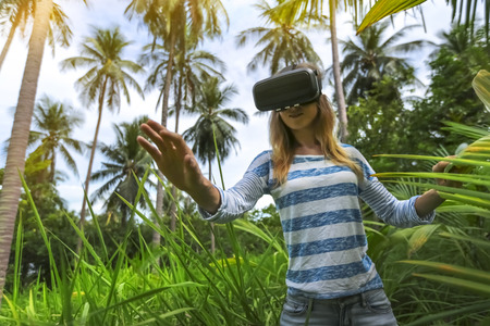 Virtual reality VR 3D headset and woman exploring the play on a background of nature jungle