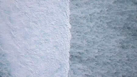 Above the ocean, aerial lock down view at foaming waves and surface near coast line