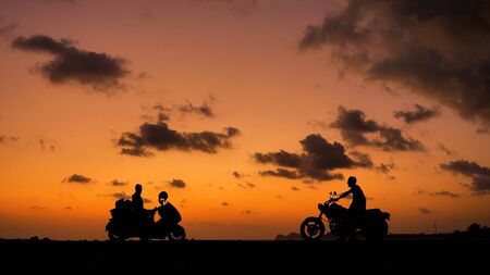People on motorcycles in silhouettes at sunset time near sea coast lineの写真素材