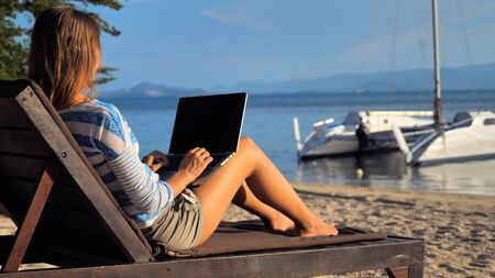 Young woman using laptop computer on a beach at tropical island. Freelance outdoor work conceptの写真素材