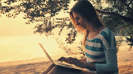 Young woman using laptop computer on a beach of tropical island. Freelance outdoor work conceptの写真素材