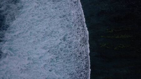 Aerial lock down view: Above the ocean, waves and water surface above coast line
