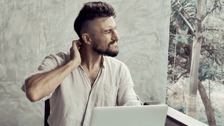A man suffering neck back pain then worked at laptop and looking overworked and stressfulの写真素材