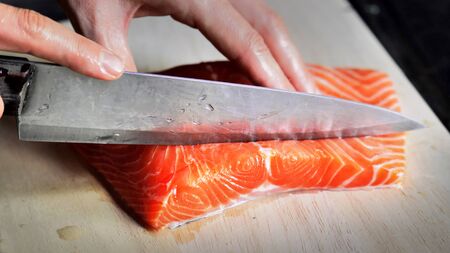 Cutting  red salmon fish with a knife at home wooden boardの写真素材