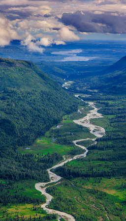 Arial picture of Alaskan tundra and dwarf forest around Denali National park, Alaska, USA. Distant glacier mountains and cloudy sky create dramatic atmosphere.の写真素材