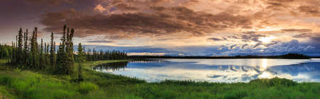 Lush green forest frames calm waters - a panoramic evening view of the Wonder Lake in Denali National Park, Alaska, USA.の写真素材