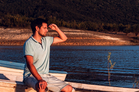 Active lifestyle outdoors. Man looking in distance, Sitting on a boat on the shore and watching the sunsetの写真素材