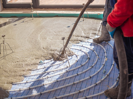 Underfloor heating and energy saving construction. Worker pouring indoor concrete screed with hoseの写真素材