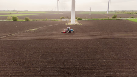 Bio vegetables and green energy. A tractor sows seeds on meadows with wind turbines at sunset...