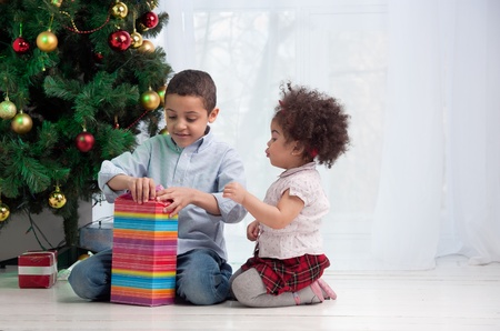 Happy children holding Christmas gifts and sitting on the floorの写真素材