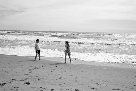 Boy and girl running and playing on beatch in front of sea. Sepia toned B&W.の写真素材