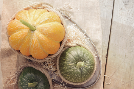 One orange pumpkin and two green pumpkin on the wooden table decorated burlap and rope. Outdoors.の写真素材