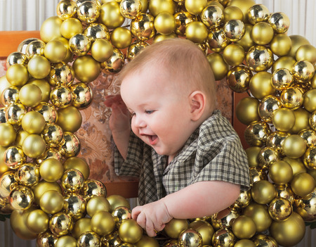 Baby boy with Christmas decor made of golden balls, indoors, horizontal.の写真素材