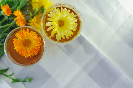 Two cups of calendula (marigold) tea on a table, with fresh flowers. Indoors. Horizontal.の写真素材