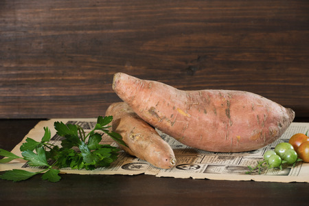 Uncooked yam fruit lying on a sheet of newspaper on a dark brown wooden background. Horizontal.の写真素材