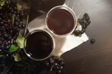 Two glasses fresh juice from black chokeberry berries ( Aronia melanocarpa ) near branches with black berries. Autumn pattern. Close-up. Top view. Horizontal.の写真素材
