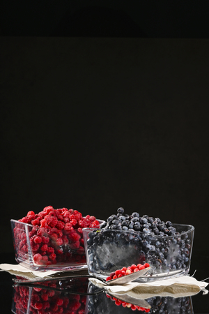 Frozen raspberry and blueberry berries in glass bowls on a dark background.の写真素材
