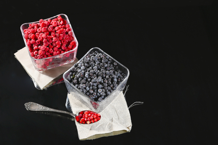 Frozen raspberry and blueberry berries in glass bowls on a dark background.の写真素材