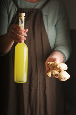 Woman holding a ginger and a bottle of homemade drink. Rustic style. Vertical.の写真素材