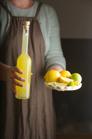 Woman holding a dish of lemon and lime and a bottle of homemade drink. Rustic style. Vertical.の写真素材