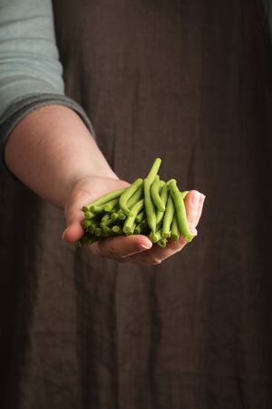 Woman holding a green beans in hand. Rustic style. Vertical.