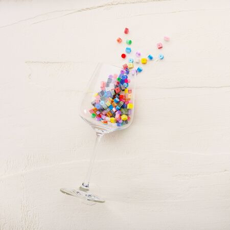 Multi-colored beads inside a wine glass on a white textured background. Flat lay.の写真素材