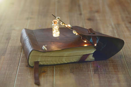 Open book with a miniature flashlight lies on a wooden table. Close-up.