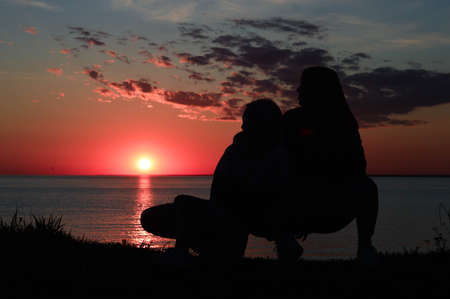 silhouettes of two girls on the shore by the sea. two girls are sitting next toの写真素材