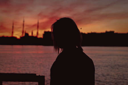 Portrait of young woman as silhouette by the sea. red sky reflected in waterの写真素材