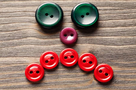 Sad face made of colored buttons on wooden table close-up macro shot, selective focus, horizontal