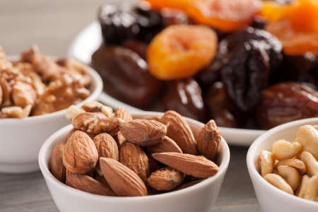 Nuts in ceramic bowls with dried fruits on a wooden table, selective focus, closeup shot
