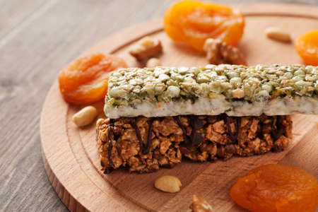 Two granola bars with dried apricots and nuts on wooden board close-upの写真素材