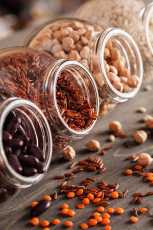 Beans and grain mix in open glass jars on a wooden table, selective focus, closeup, verticalの写真素材