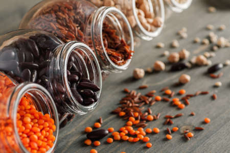 Glass jars with different grain and beans on a wooden table, selective focus, close-upの写真素材