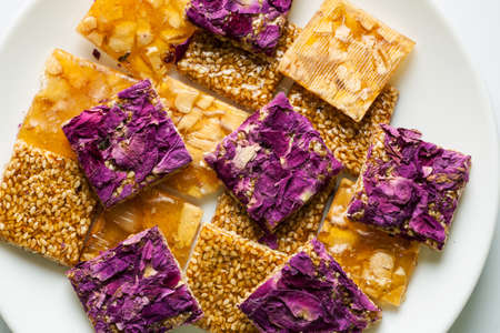 Pile of oriental sweets with nuts, seeds and rose petals in a white plate, top view, selective focus, flat layの写真素材
