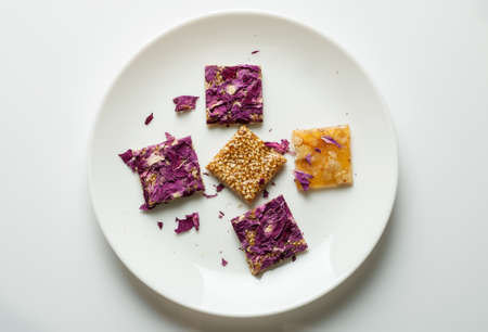 Oriental sweets with roses petals and nuts in a white ceramic plate on white background, flat lay, overhead viewの写真素材