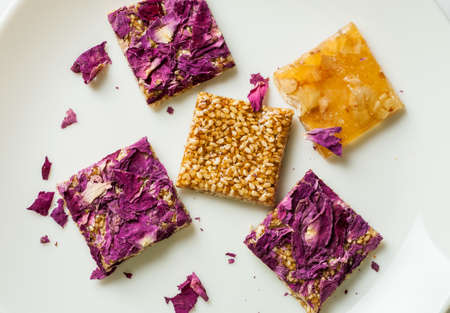Square sweets with seeds, nuts and rose petals on white, flat lay composition, overhead viewの写真素材