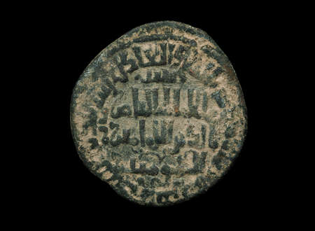 Ancient islamic bronze coin with letters on it isolated on black, close-up shotの写真素材