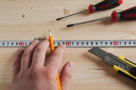 Hand with pencil and measuring tape making marks on wooden material, selective focusの写真素材