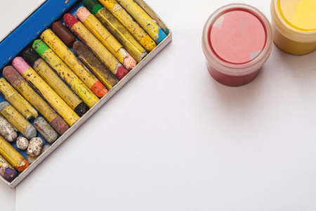 Different color crayons with two gouache jars on a white background, copy space.の写真素材