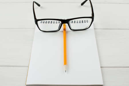 Black-rimmed glasses with open notepad and pencil on a white wooden table.の写真素材